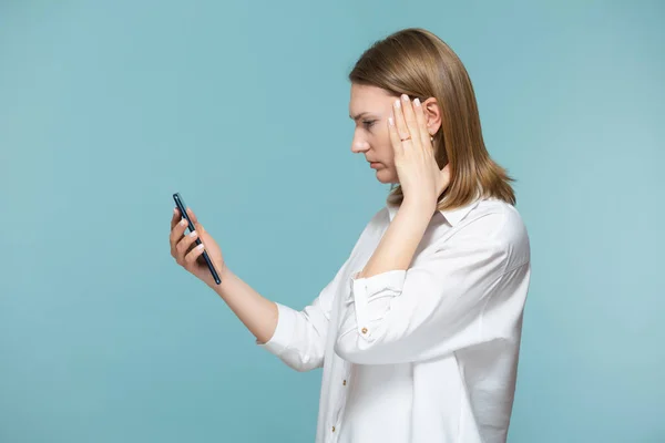 Porträt einer an Kopfschmerzen leidenden Frau, die auf blauem Hintergrund die Informationen am Telefon betrachtet. Kopierpaste. — Stockfoto