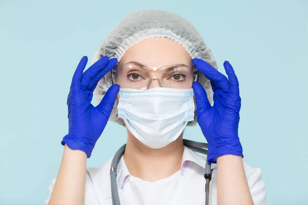 Doctor or nurse woman in a personal protective suit with a stethoscope, on a blue background. In a mask, gloves, goggles and a hat. Copy paste. healthcare concept. — Stock Photo, Image