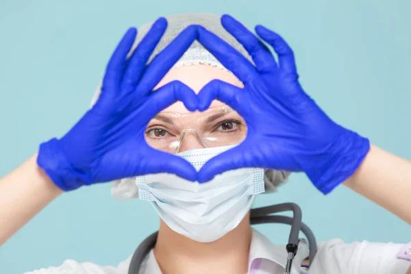 Símbolo del corazón, amor. Médico o enfermera con traje de protección personal con estetoscopio, sobre fondo azul. En una máscara, guantes, gafas y un sombrero. Copiar pasta. concepto de salud. —  Fotos de Stock