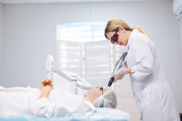 Vista lateral de la cara de una joven con gafas protectoras durante un procedimiento de pelado de carbono en un salón de belleza — Foto de Stock