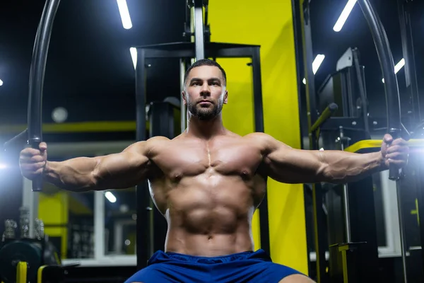 Atractivo culturista está haciendo ejercicio en un gimnasio entrenar sus músculos del pecho utilizando equipos deportivos —  Fotos de Stock