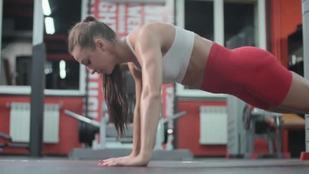 Fitness femeie musculară în pantaloni scurți roșii și alb face push-up-uri în sala de sport. ABS — Videoclip de stoc