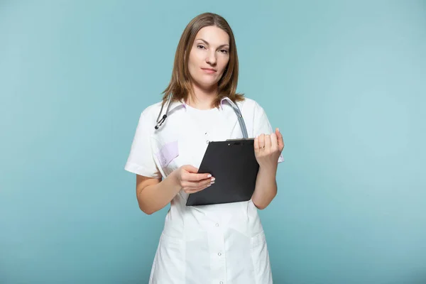 Hermosa doctora con un estetoscopio y una tableta negra, sobre un fondo azul. Copiar pasta. concepto de salud. —  Fotos de Stock