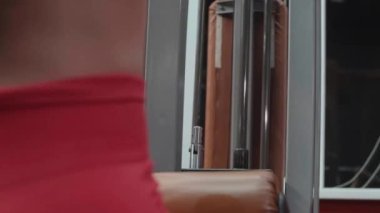 Spor salonundaki simülatörde spor yapan kırmızı şortlu ve beyaz elbiseli kaslı kadın egzersiz yapıyor. Ağırlık çalışması.