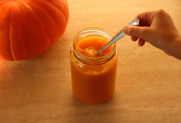 Fresh pumpkin puree in a jar with childrens hands and fresh whole pumpkin on a beige background — Stock Photo, Image