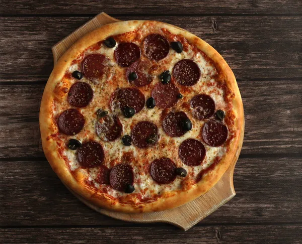 Siyah ahşap arka planda sosisli ve zeytinli biberli pizza.