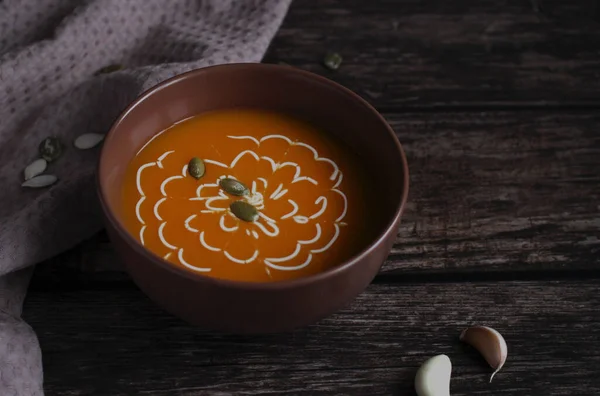 Pumpkin soup with seeds and sauce in a brown cup on a dark wooden background — Stock Photo, Image