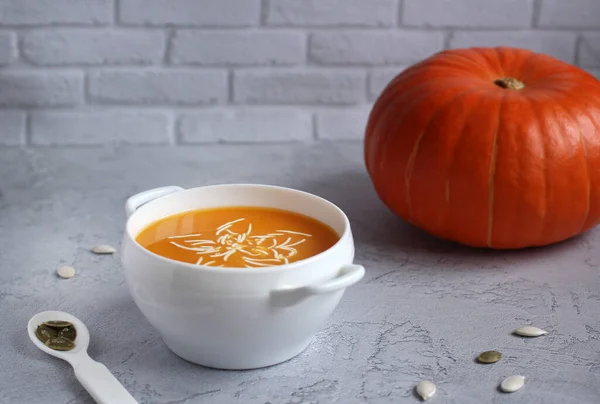 Тыквенный суп с соусом и тыквенными семечками в белой чашке на сером фоне — стоковое фото