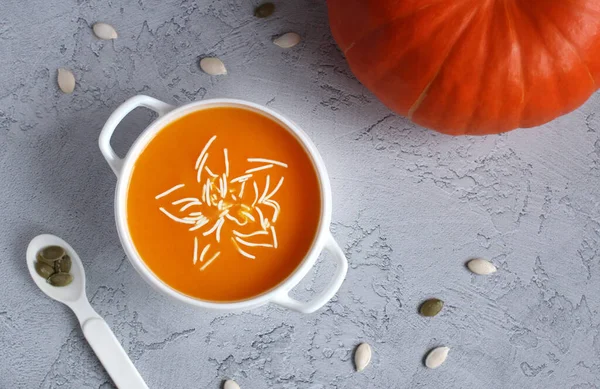 Pumpkin soup with sauce and pumpkin seeds in a white cup on a gray background — Stock Photo, Image