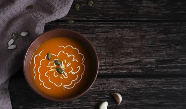 Pumpkin soup with seeds and sauce in a brown cup on a dark wooden background — Stock Photo, Image