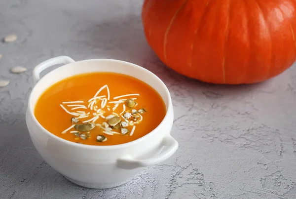 Pumpkin soup with pumpkin seeds in a white bowl on a gray background — Stock Photo, Image