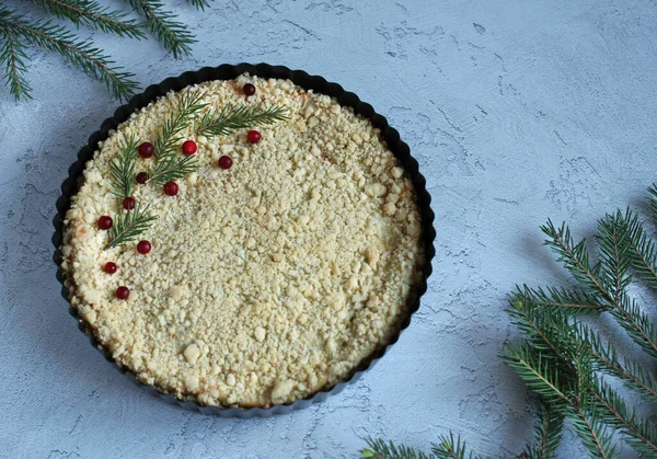 Gri-mavi arka planda ladin dalları ile siyah formda parçalanmış süzme peynirli turta.