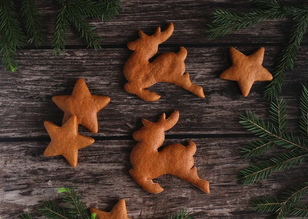 Ginger biscuits in the form of deer and stars on a wooden background with spruce branches — Stock Photo, Image