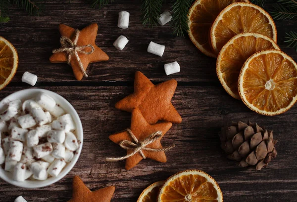 Marşmelovlu kupa, yıldızlı zencefilli kurabiye, portakal dilimleri, ahşap arka planda koniler.