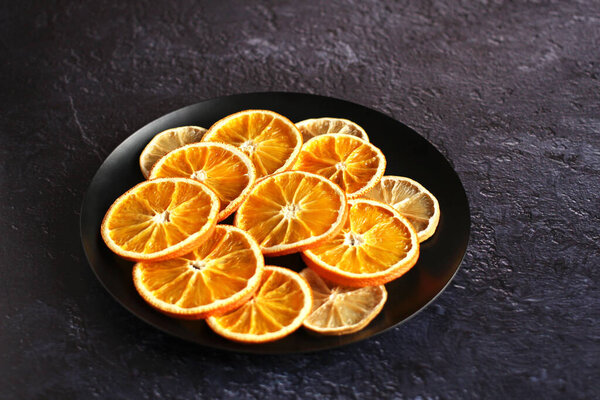 dried slices of orange and lemon fruit on a plate on a dark background with a copy space