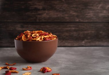 Koyu ahşap bir arka planda kahverengi bir tabakta kurutulmuş elma dilimleri.