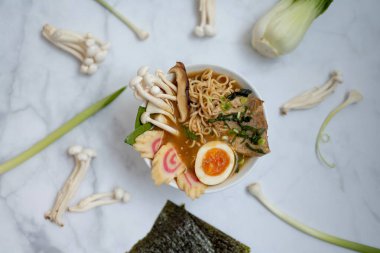 Bir kase erişte çorbası ve tüm malzemeler mermer bir masanın üzerinde.