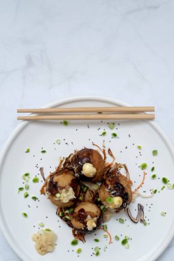 Bir tabak takoyaki ve mermer bir masanın üzerinde çubuklar.