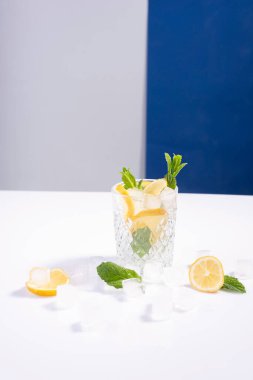Beyaz-mavi arka planda limon, nane ve buzlu buzlu bardakta buzlu yaratıcı yaz kokteyli..