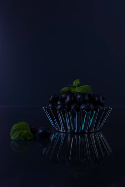 a handful of blueberries in a metal bowl on a black background..