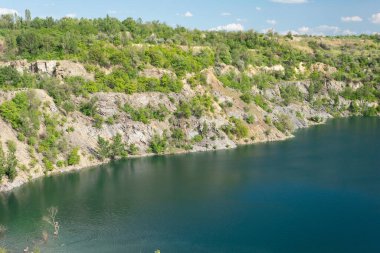 Yazın terk edilmiş granit ocağının manzarası. Sudan sarkan ağaç dalları..