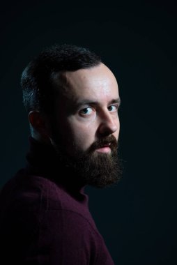 Gri arka planda bordo süveter giyen sakallı bir adamın portresi..