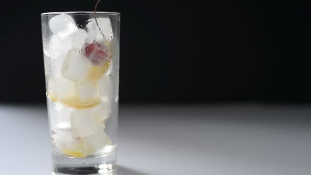 Χύνοντας λεμονάδα σε ένα ποτήρι με πάγο και φρούτα σε μαύρο και άσπρο φόντο — Αρχείο Βίντεο
