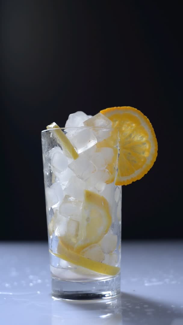 Vertikální video nalévání limonády do sklenice s ledem na černobílém pozadí — Stock video