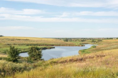 Bulutlu bir gökyüzünün arka planında nehir olan kırsal bir arazi..