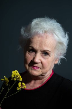 Koyu gri arka planda sarı çiçek tutan büyükannenin orijinal portresi..