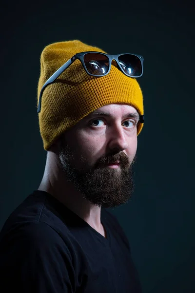 dramatic portrait of a millennial guy in a yellow hat and jacket on a dark background.
