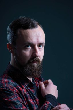 bearded guy in a plaid shirt buttoning his sleeve on a gray background.