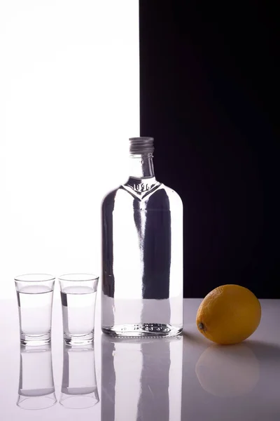 gin bottle with shot glasses on black and white background alcoholic drink with lemon.