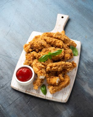 Beyaz tahta üzerinde ketçaplı kızarmış tavuk şeritleri. Fast Food