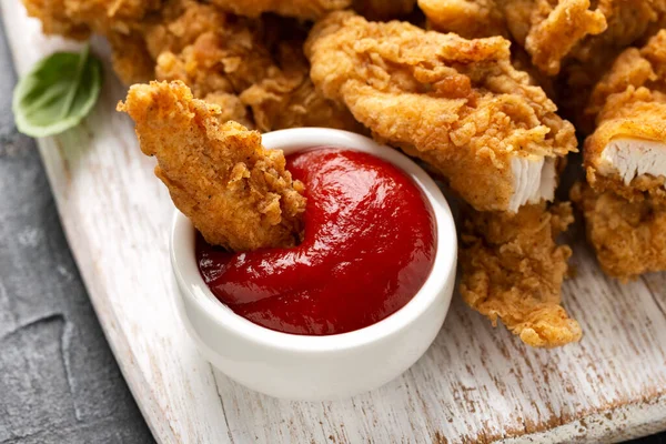 Bandes de poulet frit avec ketchup sur une planche de bois blanc. Restauration rapide — Photo