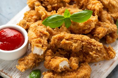 Beyaz tahta üzerinde ketçaplı kızarmış tavuk şeritleri. Fast Food