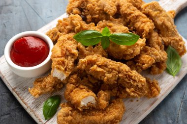 Beyaz tahta üzerinde ketçaplı kızarmış tavuk şeritleri. Fast Food