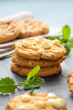 Bir bardak sütle servis edilen beyaz çikolatalı, karamel, yumuşak pişmiş kurabiyeler.