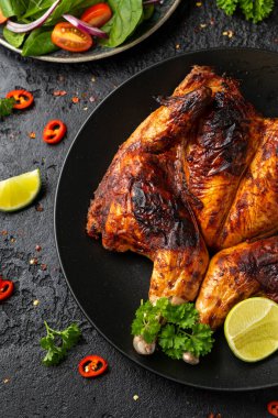 Tabaka usulü kızarmış tavuk, siyah tabakta salata, mısır ve limon..