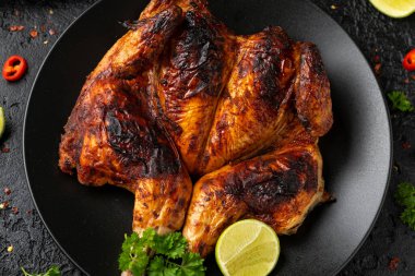 Tabaka usulü kızarmış tavuk, siyah tabakta salata, mısır ve limon..