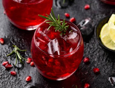 Pomegranate gin cocktail with lime, rosemary and ice on rustic black table