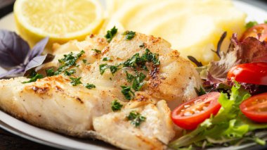 Kızarmış morina filetosu patates püresi ve taze limonla servis edilen sebze salatası..