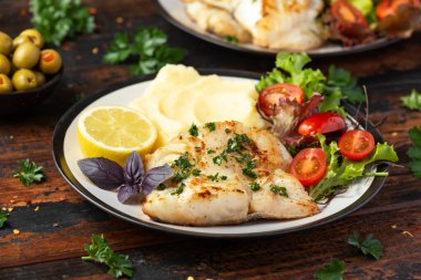 Kızarmış morina filetosu patates püresi ve taze limonla servis edilen sebze salatası..