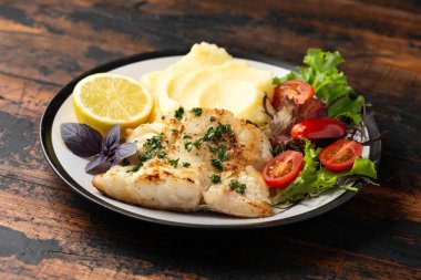 Kızarmış morina filetosu patates püresi ve taze limonla servis edilen sebze salatası..