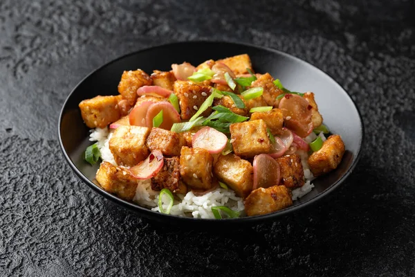 Fried tofu with radish, spring onion and garlic, ginger dressing in black bowl.