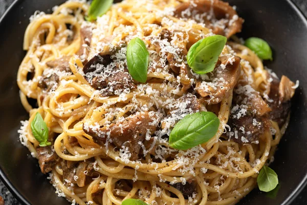 Porcini and woodland mushrooms pasta with pecorino cheese, basil in black bowl.