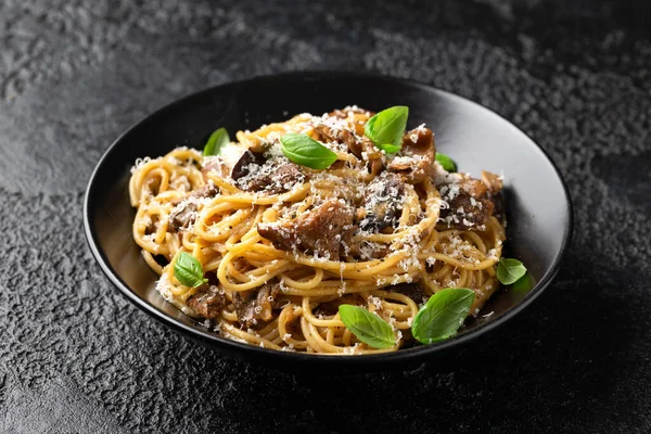 Porcini and woodland mushrooms pasta with pecorino cheese, basil in black bowl.