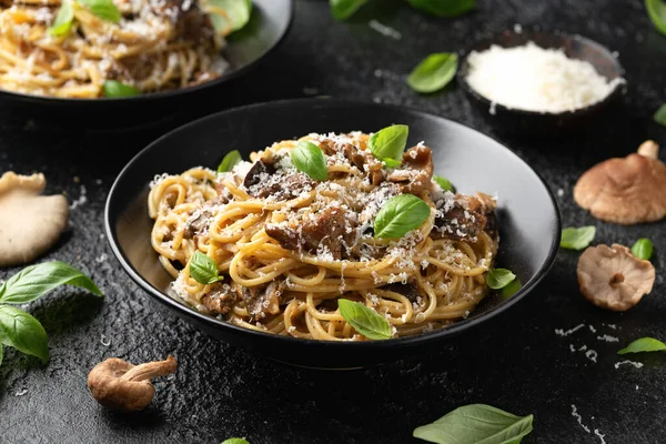 Porcini and woodland mushrooms pasta with pecorino cheese, basil in black bowl.