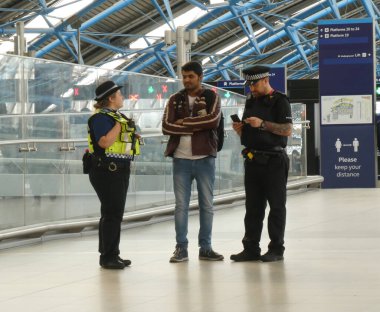 İki polis memuru Waterloo istasyonunda genç bir adamla konuşuyor.