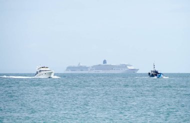 İki büyük yolcu gemisi, ön planda küçük bir balıkçı teknesi ve bir motorlu kruvazörle denize demir atmış.